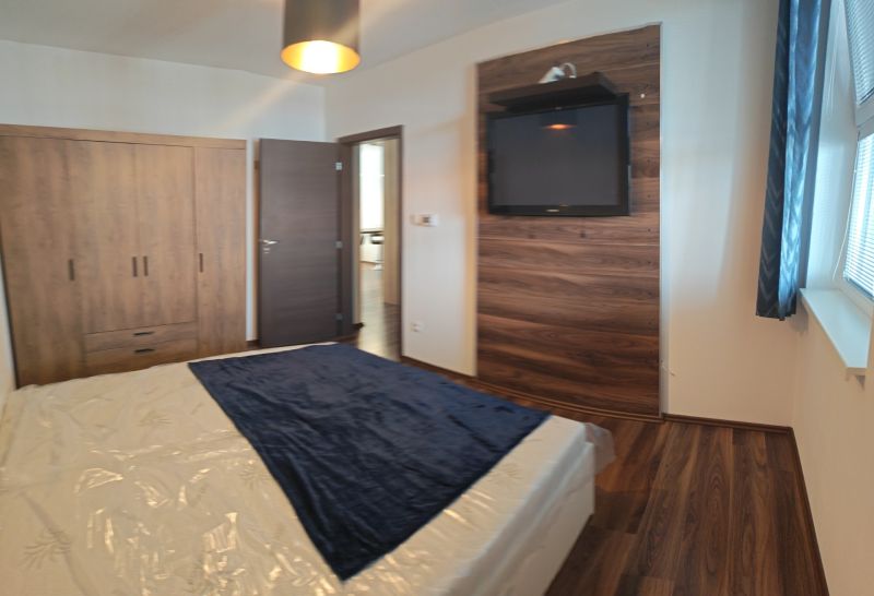 Schlafzimmer einer Zweizimmerwohnung mit Holzboden, Fernseher und Schrank.