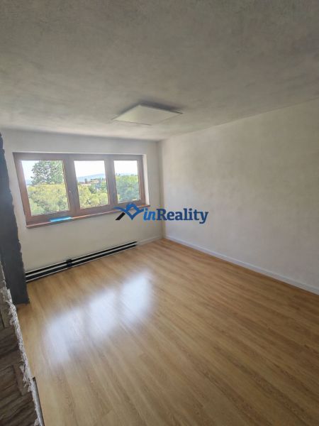 Ein Raum mit Holzboden in einem Einfamilienhaus, großes Fenster und weiße Wände.