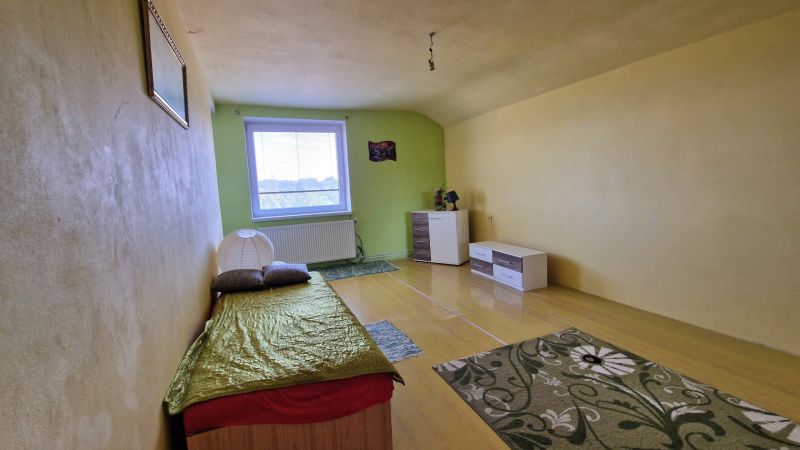 Einfaches Zimmer mit Bett, hellen Wänden und Boden in Holzoptik.