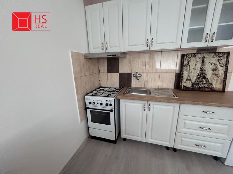 Küche mit weißen Schränken und Holzboden in einer Einzimmerwohnung.
