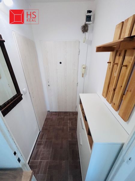 Ein schmaler Flur in einer Einzimmerwohnung mit braunem Boden und einem Kleiderständer aus Holz.