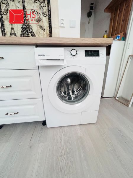 Waschmaschine in der Küche eines Einzimmerapartments mit Holzboden und Holzarbeitsplatte.
