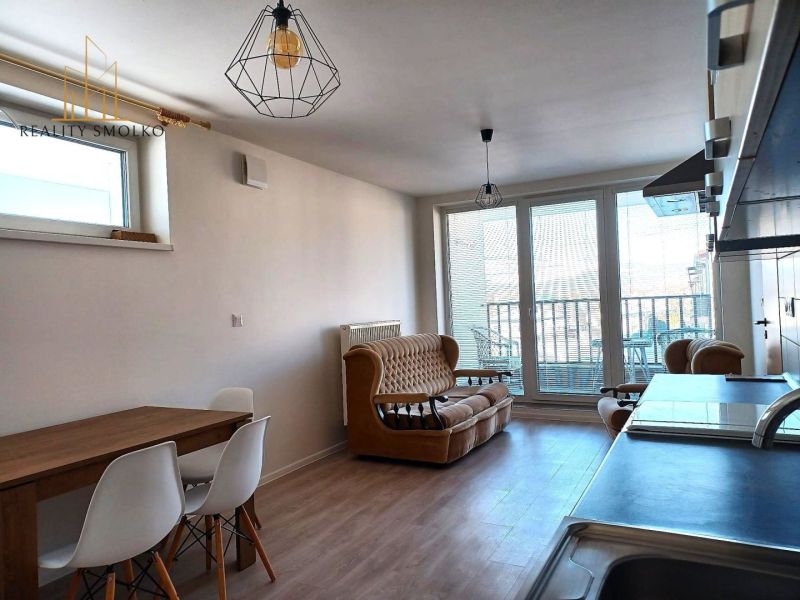 Wohnzimmer in einer Zweizimmerwohnung mit Sofa, Tisch und großen Fenstern zur Terrasse.