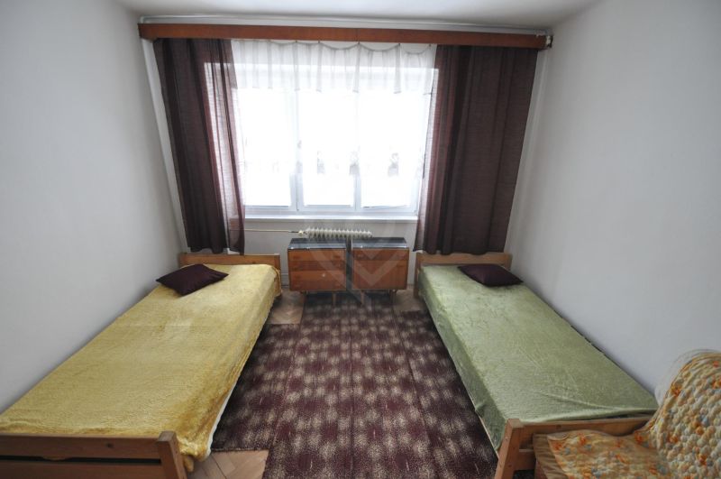 Schlafzimmer mit zwei Einzelbetten, Teppich und Fenster in einer Zweizimmerwohnung.
