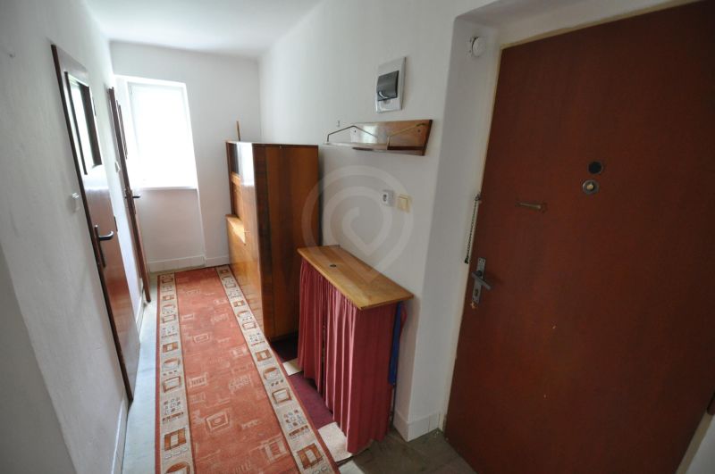 Ein enger Flur mit Teppichboden und einfacher Einrichtung in einer 2-Zimmer-Wohnung.