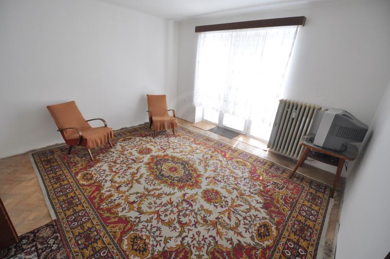 Wohnzimmer in einer Zweizimmerwohnung mit Teppich, zwei Sesseln und Fernseher.