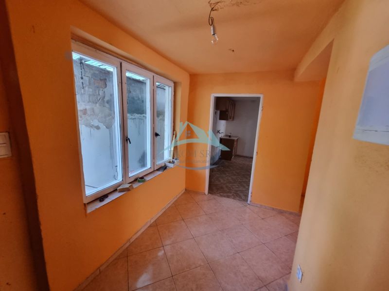 Ein orange gestrichener Flur mit Fenstern und Fliesen, der in einen weiteren Raum in einem Einfamilienhaus führt.