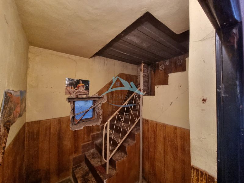 Innenraum eines Einfamilienhauses mit einer Metalltreppe, abgenutzten Wänden und einem Fenster mit Tapete.