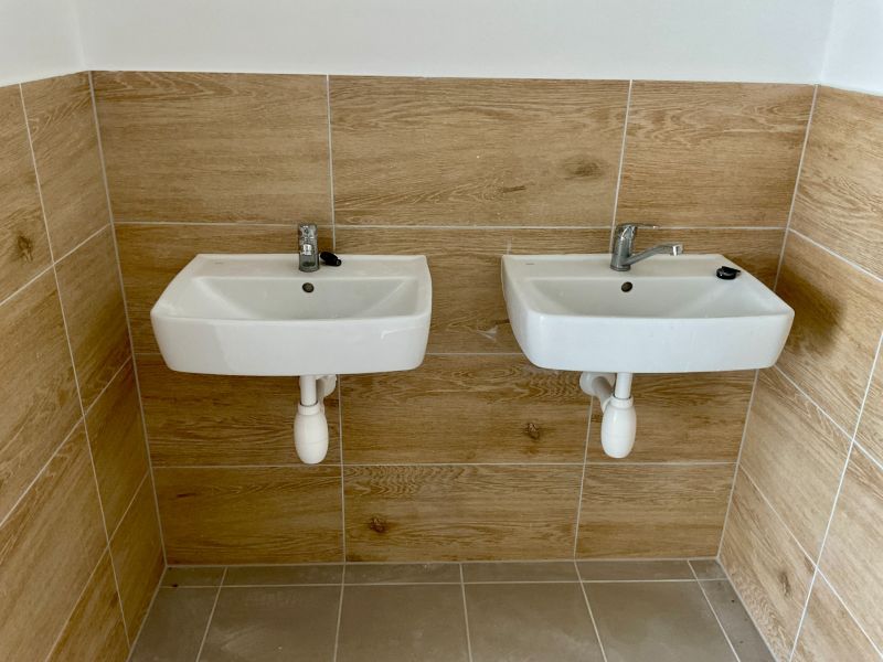 Zwei Waschbecken an der Wand mit Fliesen in Holzoptik in Lagern und Hallen.