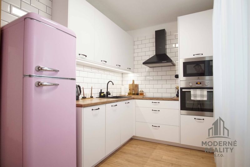 Küche in einer 2-Zimmer-Wohnung mit einem rosa Kühlschrank und einem Boden in Holzoptik.