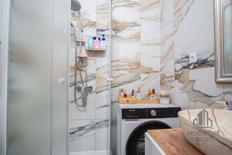 Badezimmer in einer 2-Zimmer-Wohnung mit Marmorfliesen, Duschkabine und Waschmaschine.