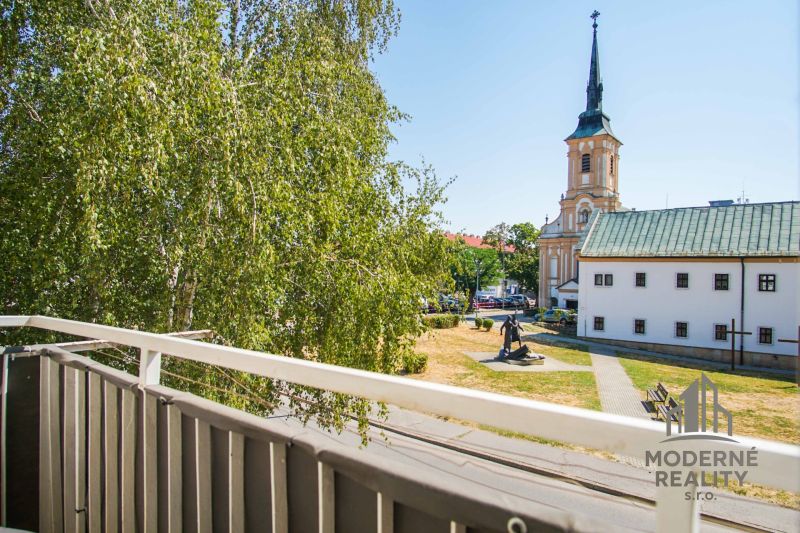 Blick vom Balkon in Nové Zámky, in der Nähe einer 2-Zimmer-Wohnung, mit Kirche und Grün.