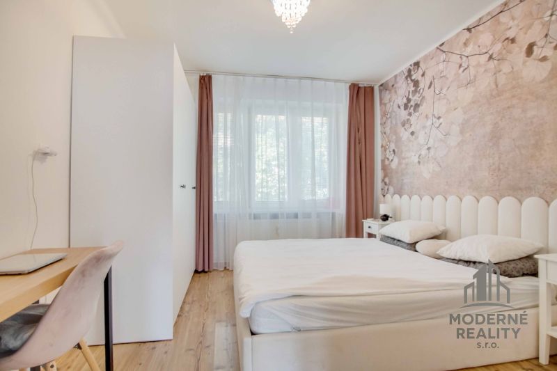 Helles Schlafzimmer mit Bett und zartem Blumendekor an der Tapete in einer 2-Zimmer-Wohnung.