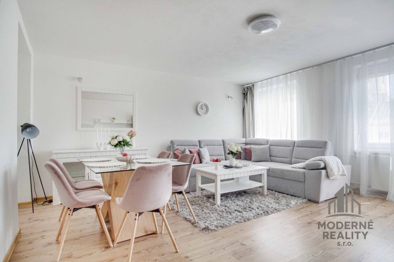Wohnzimmer in einer Zweizimmerwohnung mit Holzboden, grauem Sofa und Esstisch.