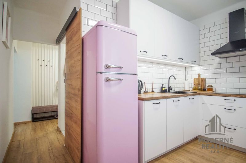 Küche in einer 2-Zimmer-Wohnung mit einem Retro-Rosa-Kühlschrank und einem Boden in Holzoptik.