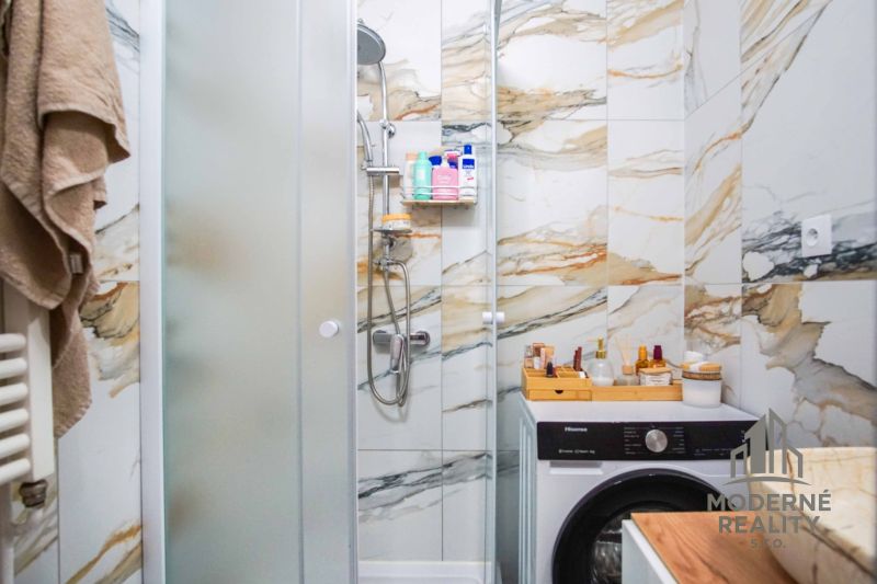 Badezimmer in einer 2-Zimmer-Wohnung mit Waschmaschine und Dusche, umgeben von Marmorbodenfliesen.