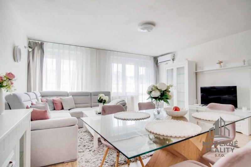 Wohnzimmer in einer Zweizimmerwohnung mit weißem Sofa und Glastisch.