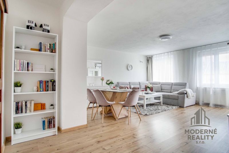 Wohnzimmer in einer Zweizimmerwohnung mit Holzboden, helle Sitzmöbel und Bücherregal.