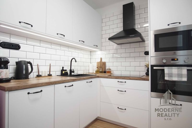 Küche in einer 2-Zimmer-Wohnung mit weißen Schränken und einem Boden in Holzoptik.
