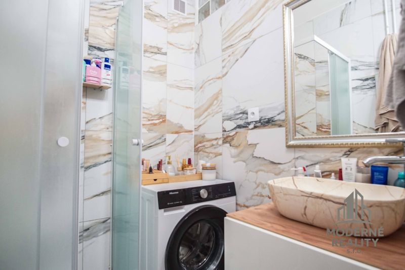 Badezimmer einer Zweizimmerwohnung mit Waschmaschine, Waschbecken und Marmorverkleidung.