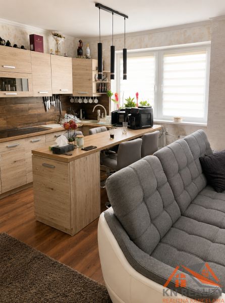 Wohnzimmer mit Küche, Holzboden, helle Schränke und graues Sofa.