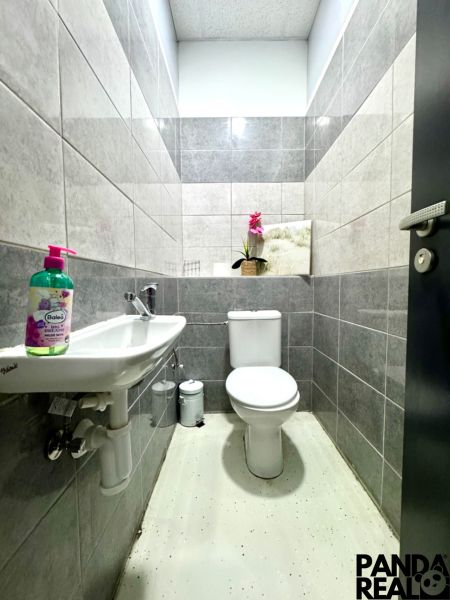 Badezimmer in Geschäftsräumen mit WC, Waschbecken und dekorativer Pflanze auf dem Regal.