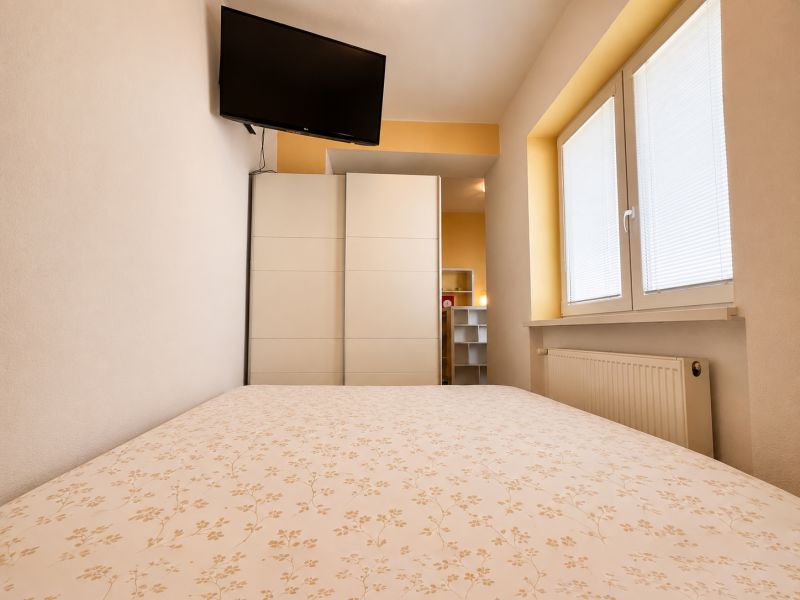 Schlafzimmer in einer Einzimmerwohnung mit Fernseher, Schrank und Fenster mit Rollläden.