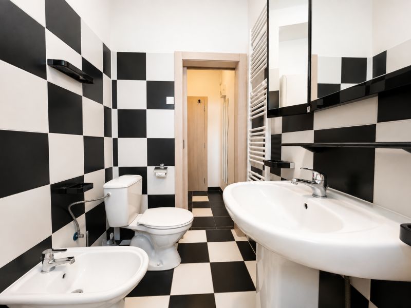 Badezimmer mit schwarz-weißen Fliesen und Keramiksanitäreinrichtungen in einer Einzimmerwohnung.