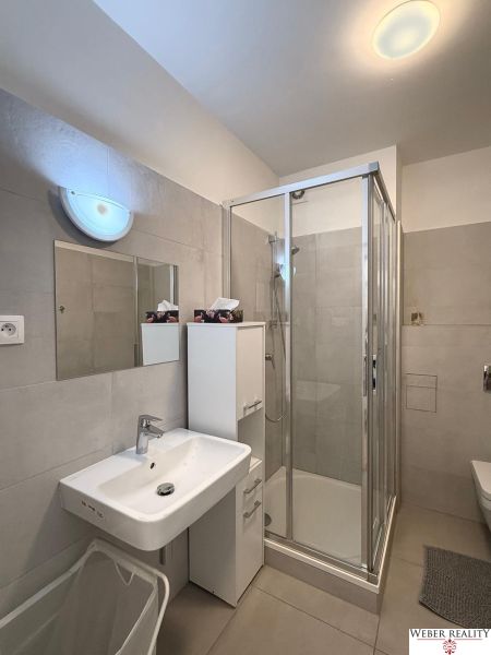Badezimmer mit Dusche, Spiegel und Waschbecken in einer 2-Zimmer-Wohnung.