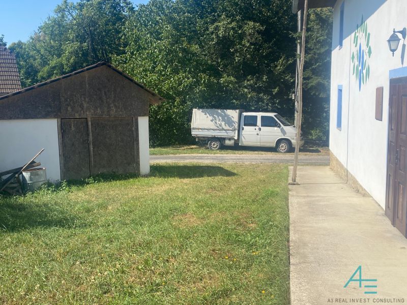 Ein Einfamilienhaus in Brestovec an der Straße mit Rasen, Unterstand und einem Lieferwagen im Hintergrund.