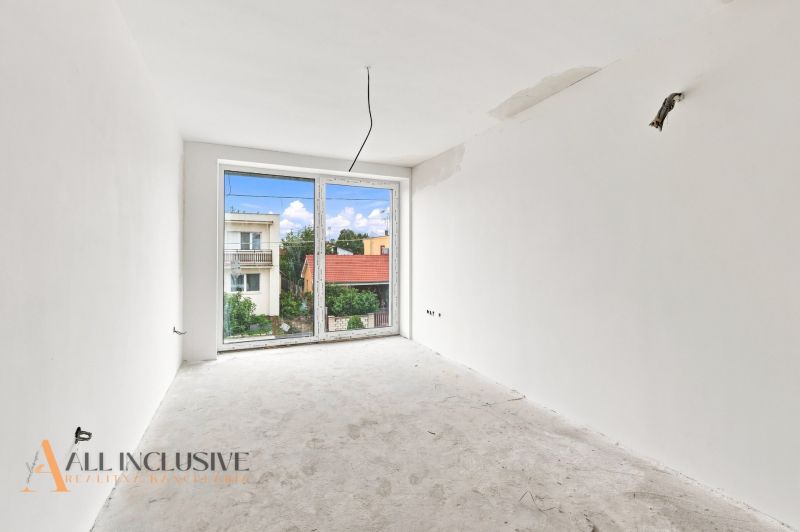 Ein unmöbliertes Zimmer in einem Einfamilienhaus mit weißen Wänden, einem großen Fenster, Blick auf den Garten.