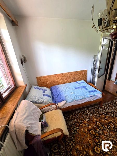 Ein Zimmer in einem Einfamilienhaus mit einem alten Teppich, einem Sessel und einem Bett am Fenster.