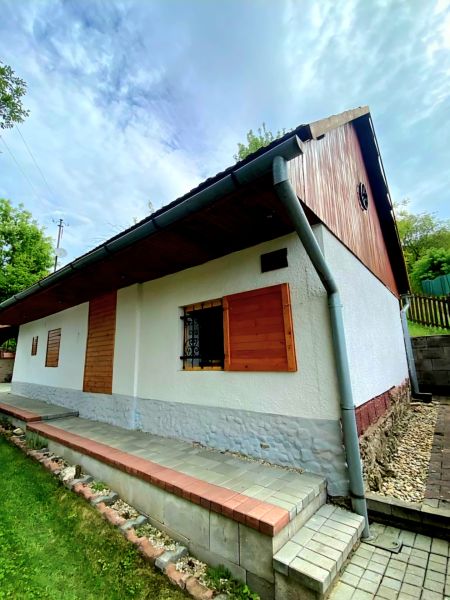 Ein Einfamilienhaus in Mikušovce mit einem Dachbelag, Holzfensterläden und einem gepflegten Garten.