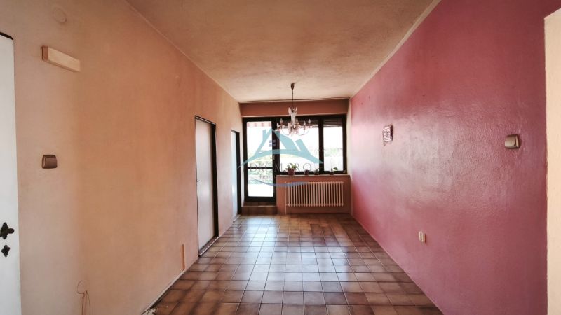Ein Flur mit Keramikfliesen, rosa Wänden, einem Fenster und einem Kronleuchter in einem Einfamilienhaus.