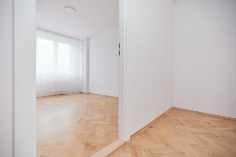 Weißes Zimmer mit großem Fenster und Holzboden in einer 3-Zimmer-Wohnung.