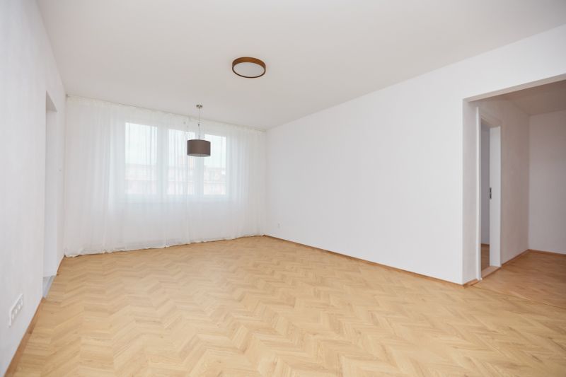 Helles Zimmer in einer 3-Zimmer-Wohnung mit Holzboden und weißen Vorhängen.