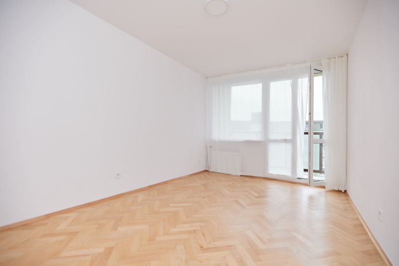 Ein leerer Raum in einer 3-Zimmer-Wohnung mit Holzboden und einem großen Fenster.