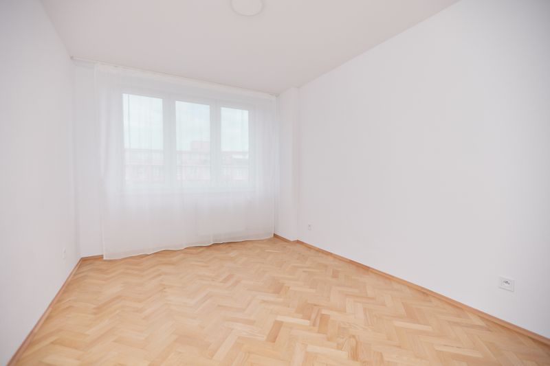 Ein leerer Raum in einer 3-Zimmer-Wohnung mit einem Holzboden und einem großen Fenster.