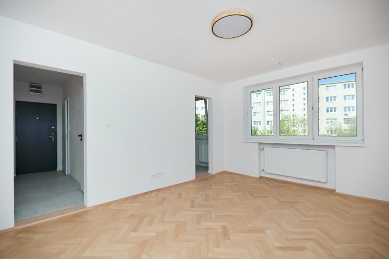 Eine Wohnung mit einem Holzboden, weißen Wänden und großen Fenstern.
