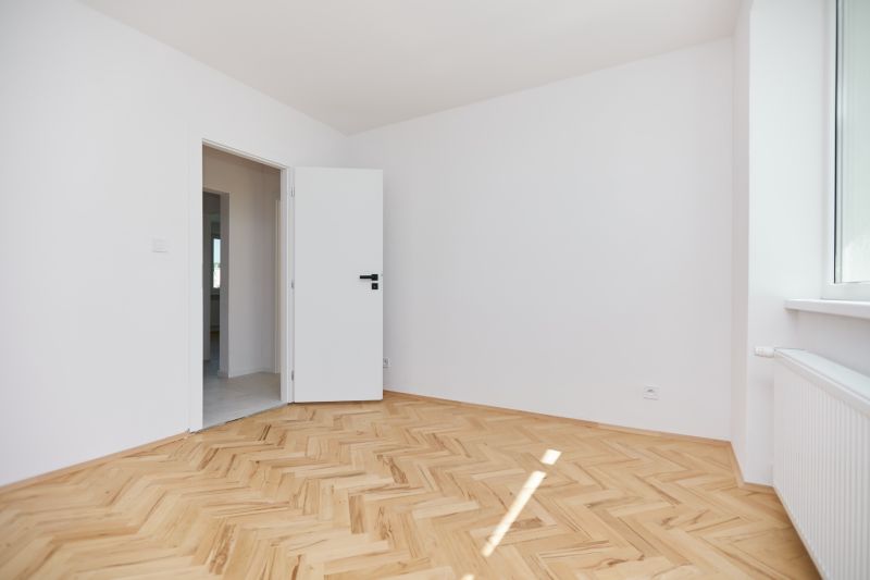 Ein Zimmer mit weißen Wänden und einem Holzboden in einer 3-Zimmer-Wohnung.