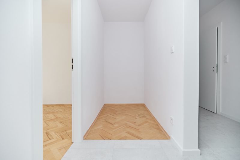 Ein enger Flur mit weißen Wänden in einer 3-Zimmer-Wohnung und einem Boden in Holzoptik.
