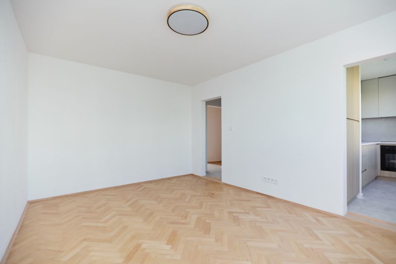 Ein leerer Raum mit Holzboden-Dekor und Blick in die Küche in einer 3-Zimmer-Wohnung.