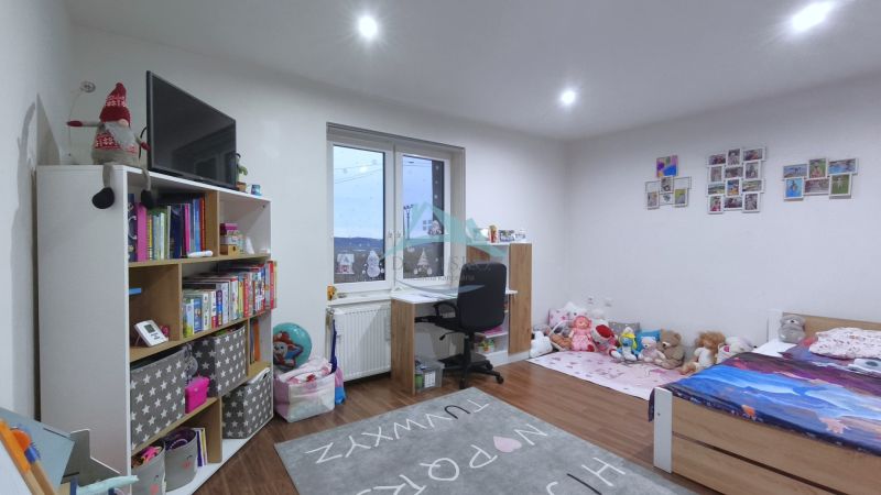 Kinderzimmer mit Bett, Schreibtisch, Regalen und einem Boden mit Holzdekor in einem Einfamilienhaus.