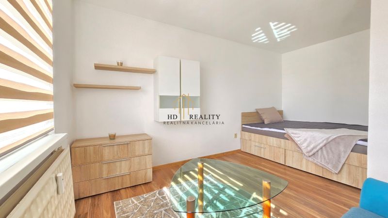 Ein Zimmer in einer Einzimmerwohnung mit einem Bett, einem Schrank und einem Boden in Holzoptik.