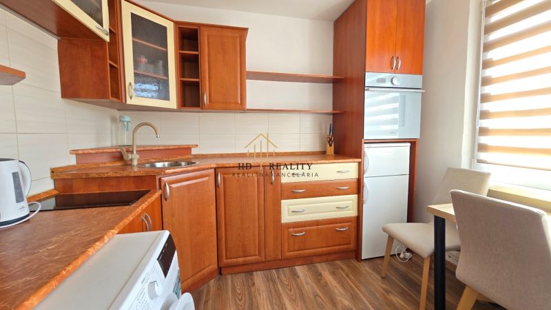 Küche in einer Einzimmerwohnung mit Holzboden und hellen Vorhängen.