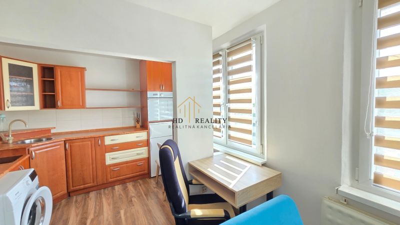 Küchenbereich mit Holzdekor, Büroecke und Waschmaschine in einem Einzimmerapartment.