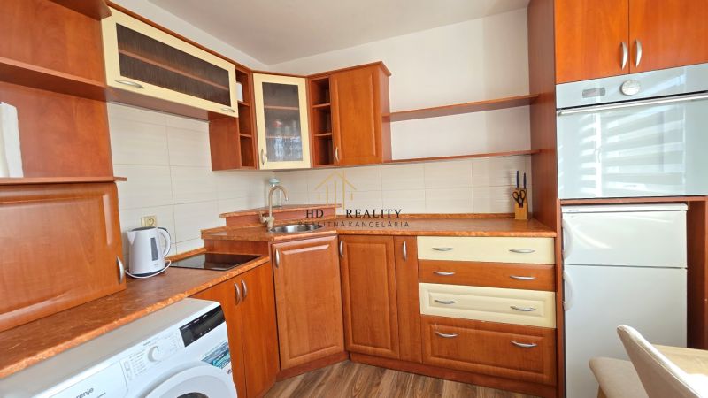 Küche mit Holzdekor in einer Einzimmerwohnung, ausgestattet mit Waschmaschine und Kühlschrank.