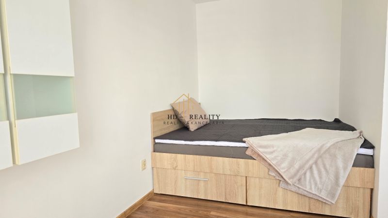 Einzelbett in einer Einzimmerwohnung mit Holzboden und Stauraum.