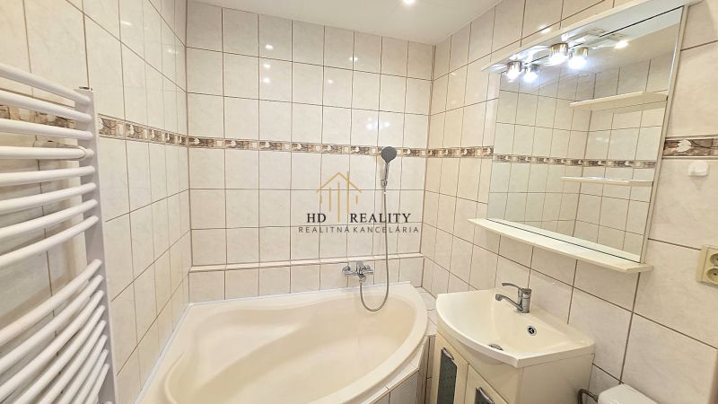 Ein Badezimmer in einer Einzimmerwohnung mit einer Eckbadewanne und einem beleuchteten Spiegel.
