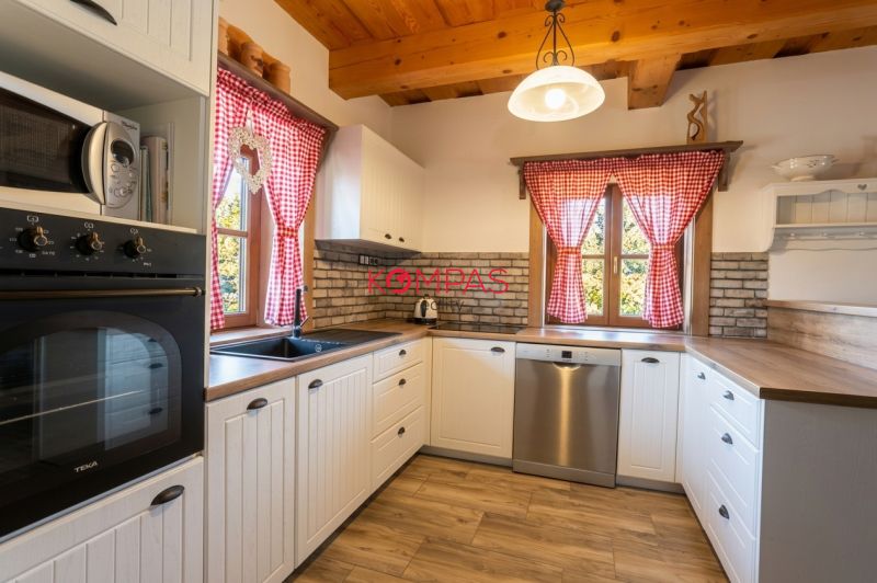 Küchenzeile in einem Einfamilienhaus mit roten Vorhängen und einem Boden in Holzoptik.